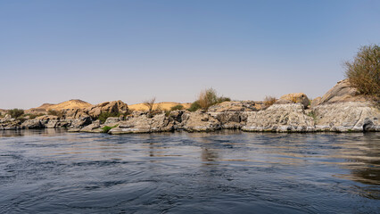 Fototapeta na wymiar A blue calm river with rocky shores. Picturesque boulders and sand dunes against a clear sky. Ripples and reflections on the water. Copy space. Egypt. Nile