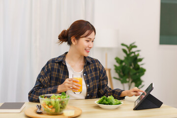 Obraz na płótnie Canvas Lifestyle in living room concept, Young Asian woman touching on tablet and drinking orange juice