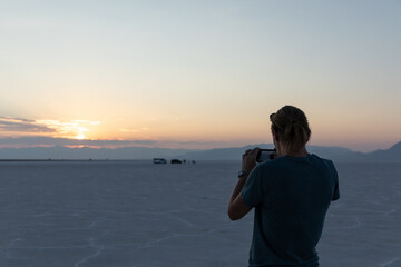 Young woman taking a photo of sunset on Bonneville Salt Flats in Utah