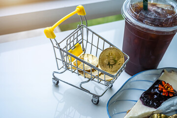 Close-up of Golden bitcoins or cryptocurrency coin or symbols in shopping cart and Americano iced coffee or black and Blueberry Cake in white table. Future currency concept.