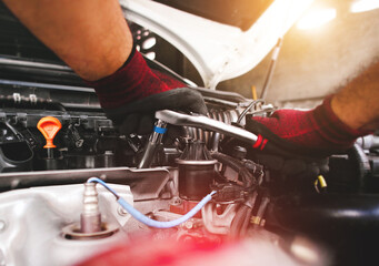 The red gloved hand of the auto mechanic is fastening the bolt with the socket wrench to fix the...