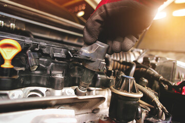 A auto mechanic is installing  ignition coil for a spark plug into the ignition socket of the engine block in the engine compartment. - obrazy, fototapety, plakaty