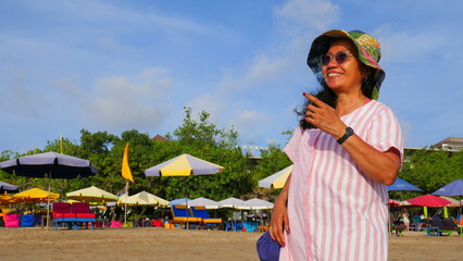charmant lächelnde Asiatin spaziert in Bali entlang des Strandes mit Sonnenschirmen bei blauem...