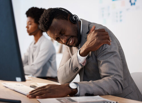 Pain, injury and hurt call center agent holding his shoulder in agony while working in the office. Young African American male customer service consultant suffering from a painful arm