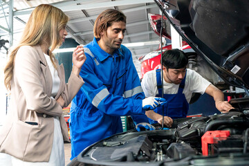 Fototapeta na wymiar Male car operator wearing blue overalls, gloves working under the hood of car and checking attentively serviceability of engine at repair garage. Concept of car maintenance