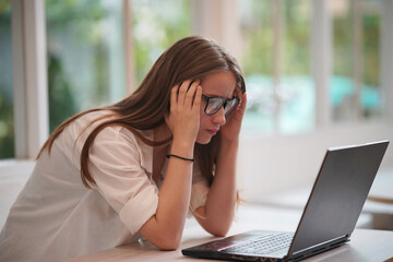 Indoor shot of young woman looking at laptop seriously. Female sitting at home office and working on laptop computer.