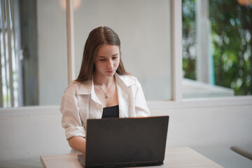 Technology and people concept, young woman using laptop and internet technology and sitting on the desk with laptop computer.