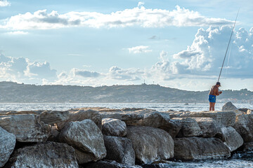Signore intento a pescare sugli scogli in riva al mare