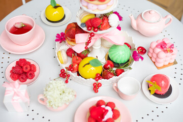 Serving festive table of appetizing cakes, sweet desserts, fresh strawberry and raspberry, tasty drinks top view. Party in pink style, holiday celebration, luxurious service, cute tableware