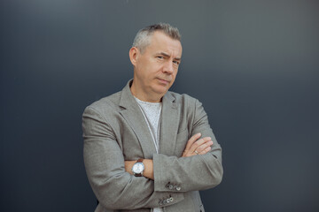 Portrait of successful aged gray haired businessman standing with crossed arms in stylish suit and...