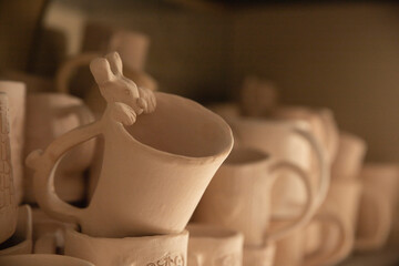Clay mugs made of clay molded by hand and decorated with ornaments. Unpainted handmade pottery displayed in rows close-up.