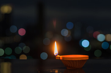 Selective focus on the flame of clay diya lamp with colorful city bokeh lights. Diwali festival...