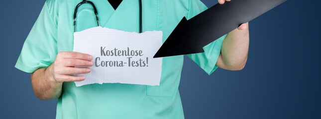 Kostenlose Corona-Tests!. Arzt hält Zettel und zeigt mit Pfeil auf medizinischen Begriff.