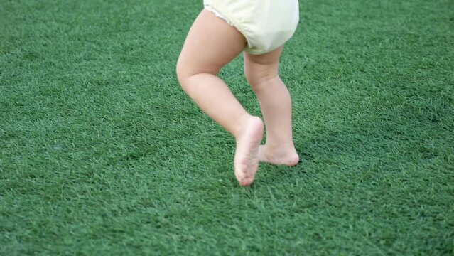 Toddler boy legs learn to walk on green grass running without stopping. Small kid imagines himself runner playing on big stadium on dull day