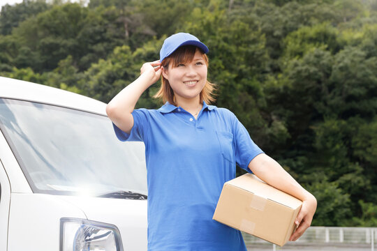 軽貨物自動車のドライバー。青いポロシャツと帽子を着て段ボールを運んでいる女性。