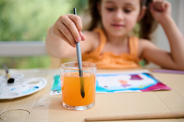 Selective focus on a glass with colored water and hand of blurred Caucasian child, preschooler girl...