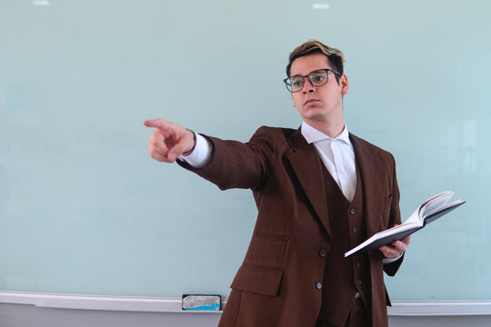 University professor with the white board behind giving a class pointing somewhere. Elegant man in a suit pointing at the students at him. Teacher giving class. High quality photo - Powered by Adobe