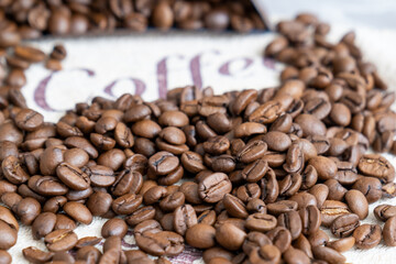 Fototapeta premium scattered coffee beans on a table, next to word coffee, coffee culture, Space for text. Good picture for cover, calendar, postcard, wallpaper, background, product, website, blog, business, magazine