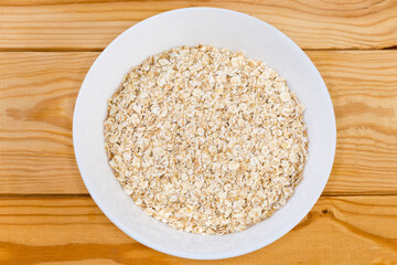 Raw rolled oats in bowl on rustic table, top view