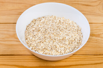 Raw rolled oats in bowl on rustic table, close-up