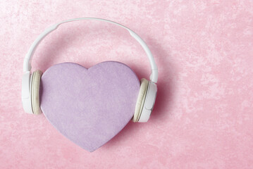 Heart shaped gift box in headphones over pink stone background