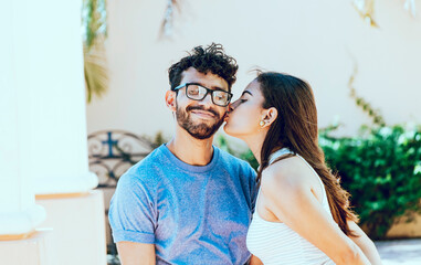 Girl kissing her boyfriend on the cheek while smiling. Young woman kissing her boyfriend on the cheek in the street. Concept of happy girlfriend kissing cheek of her boyfriend outdoors