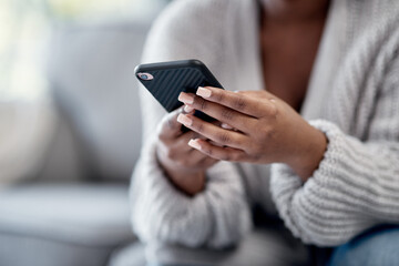 Closeup of woman hands typing on phone, sending a text message online on social media on home sofa. Female reading and replying to a work email. African American lady playing a game on mobile device.