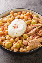 Lablabi or lablebi is a Tunisian soup containing chickpeas and it is served over pieces of stale bread and topped with a poached egg and tuna closeup in the bowl on the table. Vertical