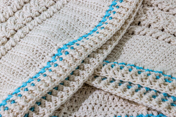 Close-up of a beige cotton yarn crochet blanket with a braided pattern and blue details on the...