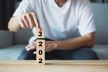 Young man wearing white t-shirt using hand flipping wooden cubes blocks for change year 2022 to...