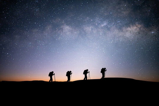 Silhouette of four young traveler and backpacker hiking to the top of the mountain with beautiful view star, milky way over the sky. He enjoyed traveling and was successful when he reached the summit.