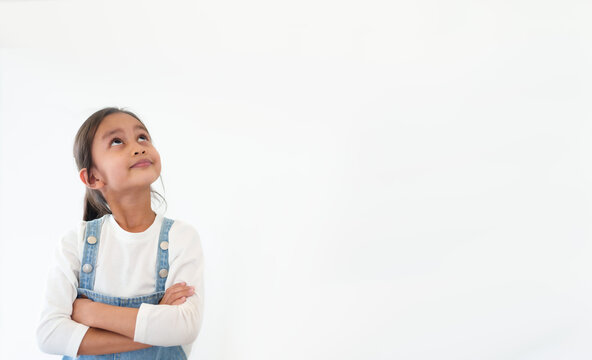 Isolated of happy and healthy 6 years old asian little girl is standing and looking up on the white background. Concept of thinking, idea, expression, advertising, people, lifestyle.