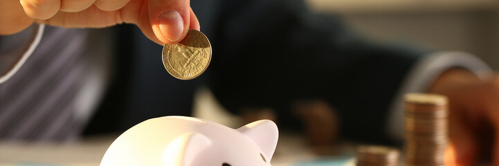 Businessman hand throws a coin into piggy bank