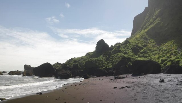 Vik, Iceland with black sand beach and green mountains with gimbal video walking forward.