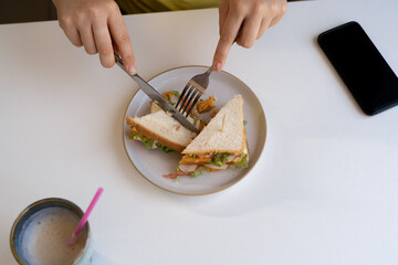 Woman eating a sandwich for lunch in a restaurant or cafe, cutting with a knife and fork