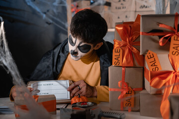 start up business owner packing cardboard box at workplace. man in a skull make-up prepares a...