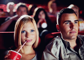 Couple in dark movie theatre, drinking cola on date in cinema and man and woman watching a film together for entertainment. Face of happy, dating and fun boyfriend and girlfriend at the movies