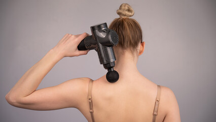 Caucasian woman giving herself a back massage with a gun. 