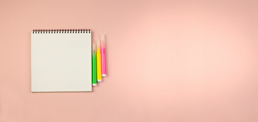 Notepad on a black spring and markers on a pink background. 