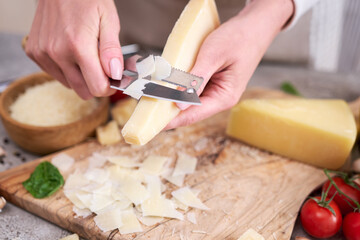 Woman slicing Parmesan cheese on a wooden cutting board at domestic kitchen