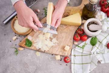 Woman slicing Parmesan cheese on a wooden cutting board at domestic kitchen
