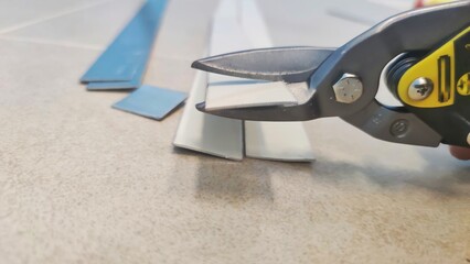 A locksmith in the workshop cuts a metal plate with scissors