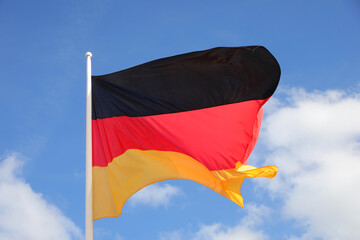 Waving big flag of Germany in Europe on blue sky