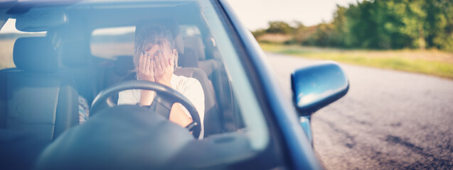 Upset woman sitting in the car and covering face with her hands