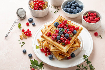 Traditional belgian waffles with fresh berries, raspberries, currant, blueberries, maple syrup, thyme on pink background. Summer concept. Selective focus.