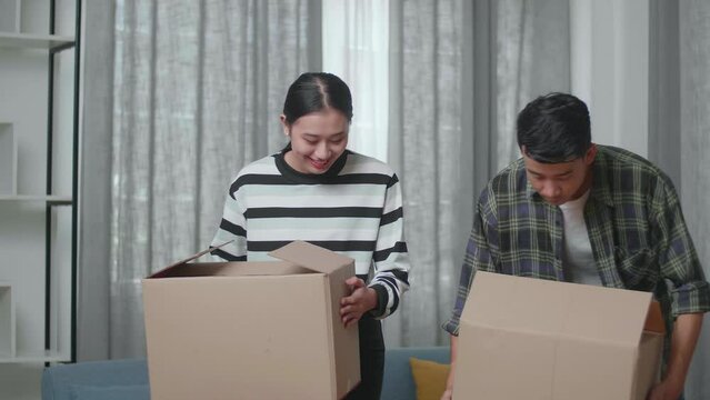 Smiling Young Asian Couple Carrying Cardboard Boxes With Stuff Into A New House Then Looking Around
