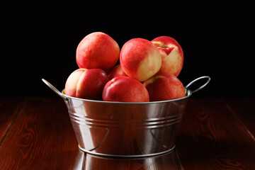 Ripe red nectarines in a tin bowl on a black background. Side view.
