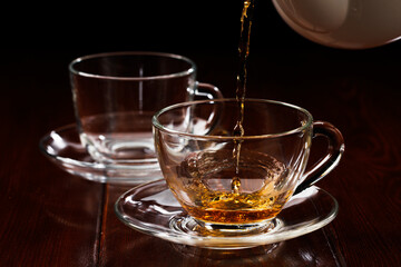 A jet of tea at the beginning of pouring into a glass cup. Selective focus.