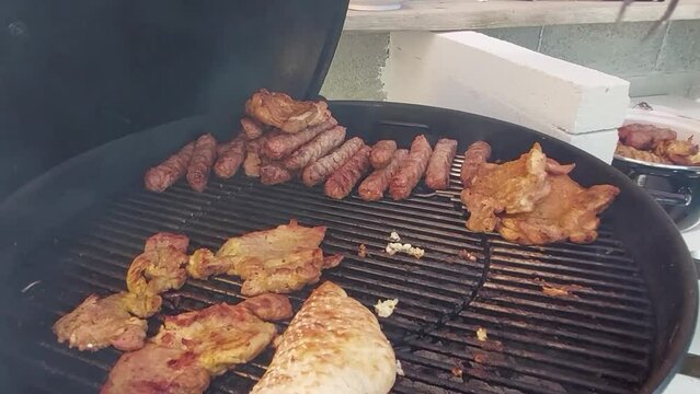 Taking off minced meat fingers called cevapcici from charcoal grill with steel clamps.