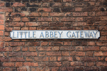 Faded street name sign for Little Abbey Gateway mounted on a red brick wall